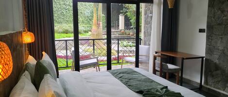 Une chambre d’hôtel avec un grand lit, une petite table et un balcon donnant sur un jardin.