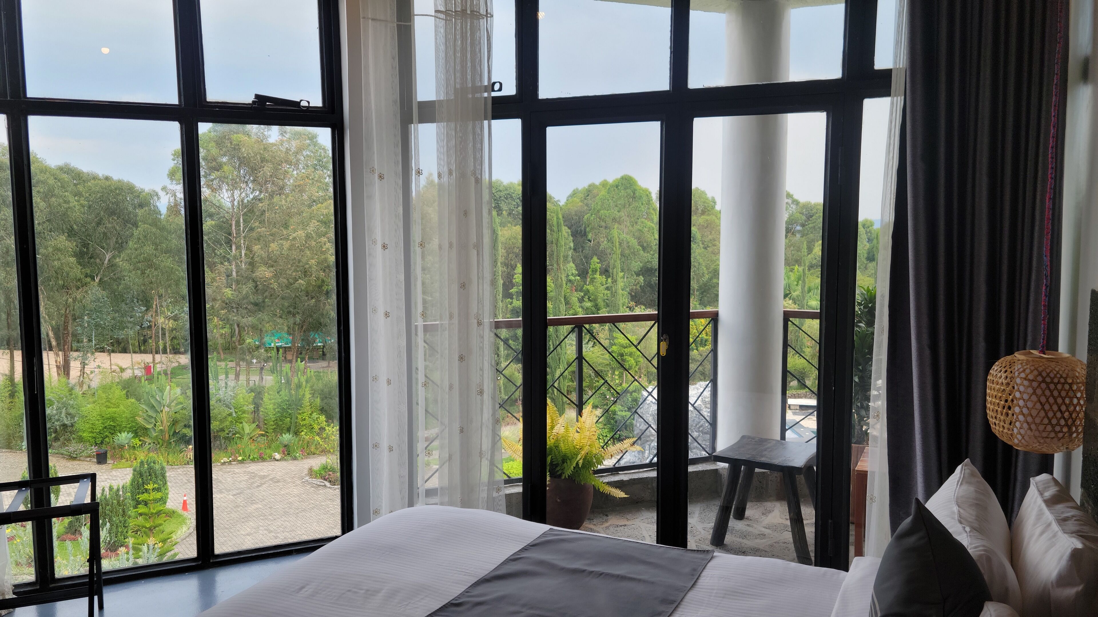 Una stanza con ampie finestre, un letto, una pianta in vaso e vista su un giardino e degli alberi.