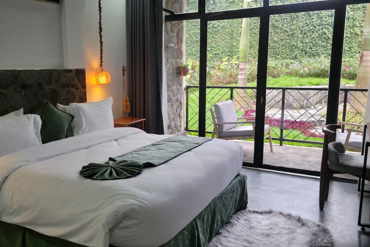 A bedroom with a large bed, a stone accent wall, a hanging light, and a view of a garden through a glass door.