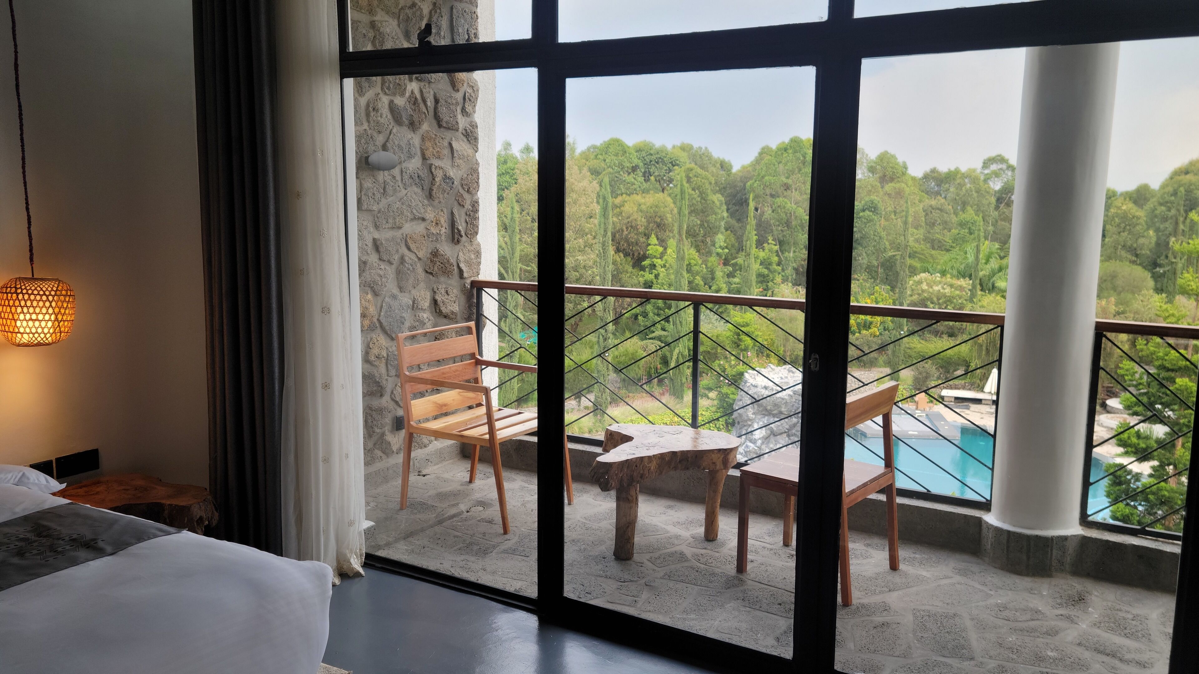 A balcony with a stone wall, wooden furniture, and a view of a swimming pool.