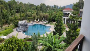 Un resort con una amplia piscina rodeada de exuberante vegetación y montañas al fondo.