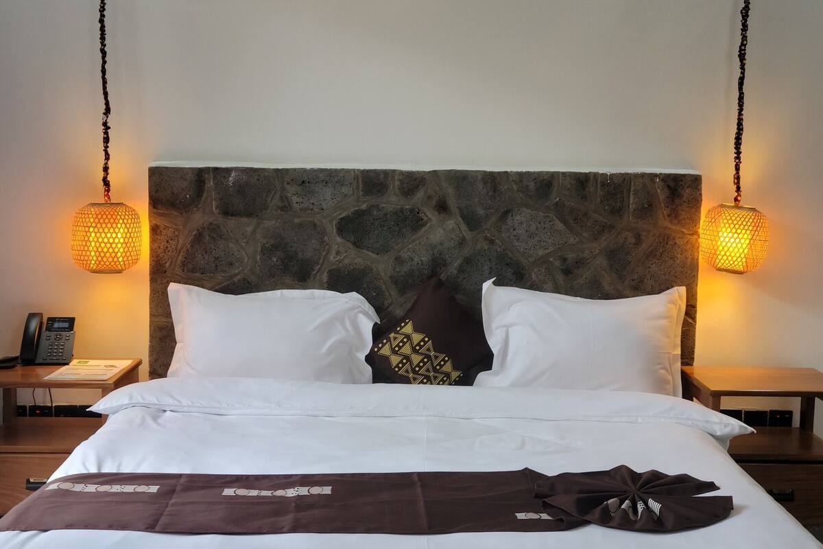 A neatly made bed with white and brown bedding, a stone headboard, and two hanging lamps on either side.