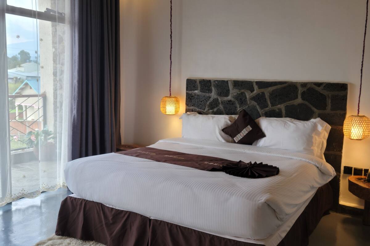 A neatly made bed with white linens, a stone headboard, and two wall-mounted lamps.