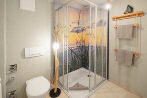 Baño con ducha de vidrio, inodoro, toallero e interruptor de luz.