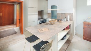 Une cuisine moderne dotée d’un plan de travail en marbre, de deux tabourets de bar, d’un four encastré et d’un évier.
