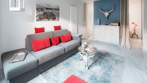 A modern living room with a grey sofa, red cushions, a glass coffee table, and a blue patterned rug. - // VACATION APARTMENT BARKE 03 // (Norderney)