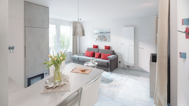 A modern kitchen with a large island, a grey sofa with red cushions, and a vase of tulips. - // VACATION APARTMENT BARKE 03 // (Norderney)