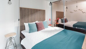 A modern hotel room with a large bed, a small stool, and a mirror. - // VACATION APARTMENT BARKE 03 // (Norderney)