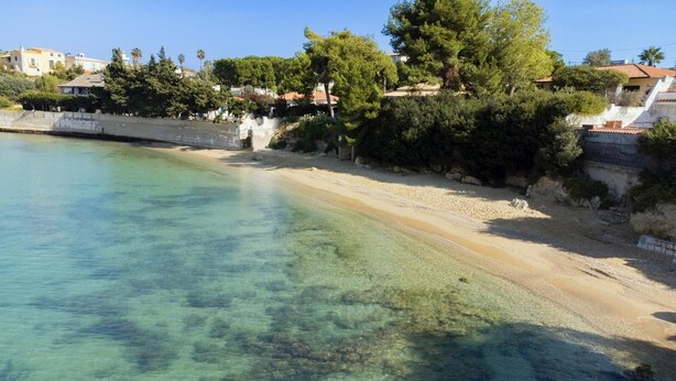 Platja costanera amb aigua cristal·lina, sorra daurada i edificis residencials al fons.