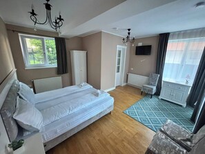 A hotel room with a double bed, a TV, a radiator, a window with curtains, a door, and a small table with a chair. - Premont Guesthouse Bran (Bran)