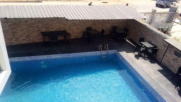 Una piscina rectangular amb vora de rajola, envoltada per una paret de maó i un sostre metàl·lic. Hi ha gandules i una taula a l'exterior de la zona de la piscina.