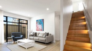 A modern living room with a sofa, armchair, coffee table, and a large window. - Townhouse on Tod Glenelg North (Glenelg North)