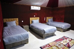 A room with three beds, each with a wooden headboard and a grey bedspread. There is a red patterned wall and a patterned rug on the floor. - Rum Pillars Camp (Wadi Rum)