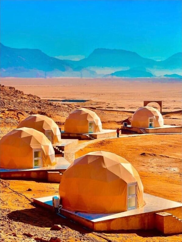 A desert landscape with multiple dome-shaped structures, likely accommodations, with a clear sky and distant mountains. - Rum Pillars Camp (Wadi Rum)