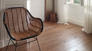 A room with a wooden floor, a wicker chair, a mirror, and a window with curtains. - A Magnagnerie in Provence (Bouchet)