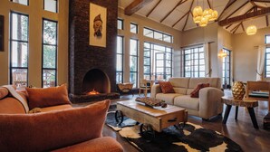 A spacious living room with a fireplace, large windows, and rustic decor. - Kaara Gorilla Mountain Lodge (Bugambira)