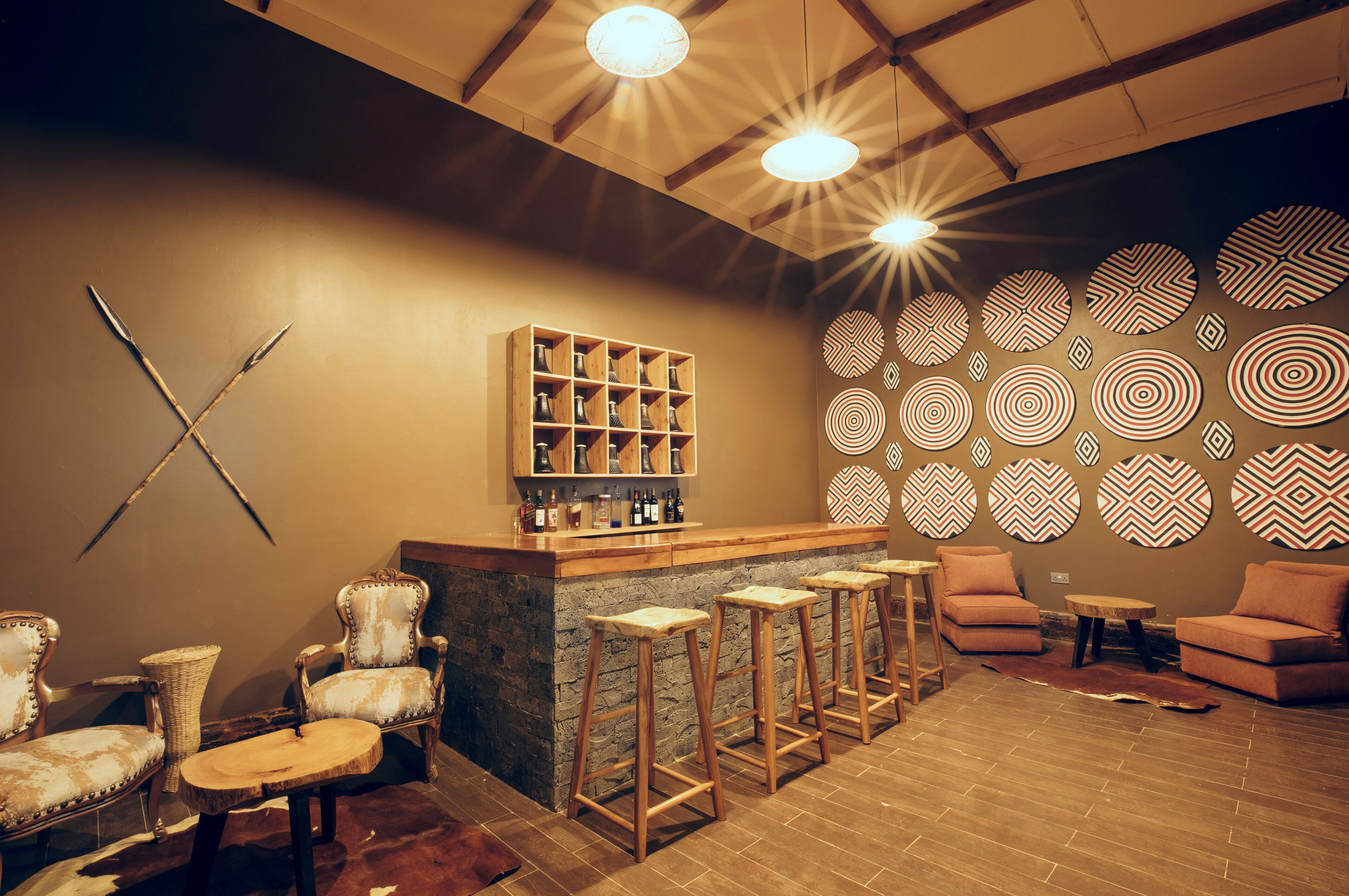 A bar area with stools, a wooden shelf with bottles, and a patterned wall.