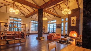 A spacious living area with high ceilings, exposed wooden beams, and large windows. There is a fireplace, a sofa, and a coffee table. - Kaara Gorilla Mountain Lodge (Bugambira)
