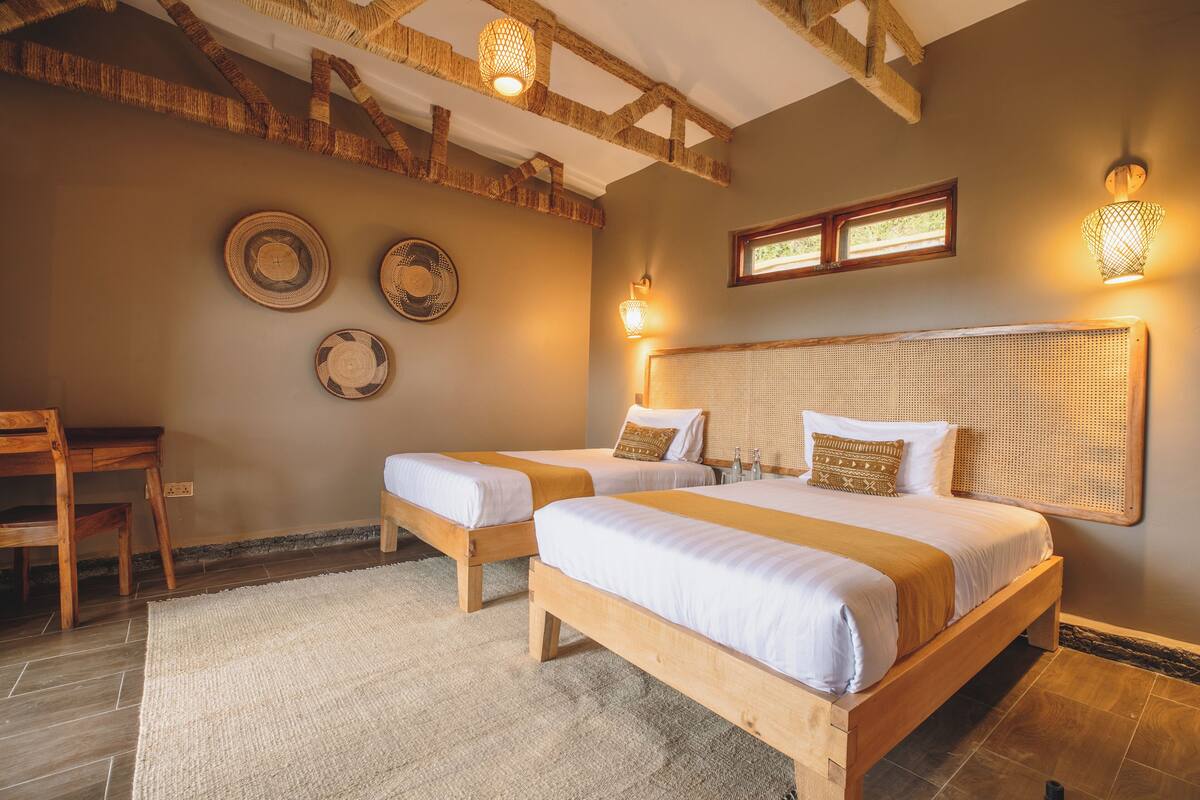 Habitación con dos camas de madera, un escritorio y una silla. Cuenta con luces en la pared y una ventana con vistas.