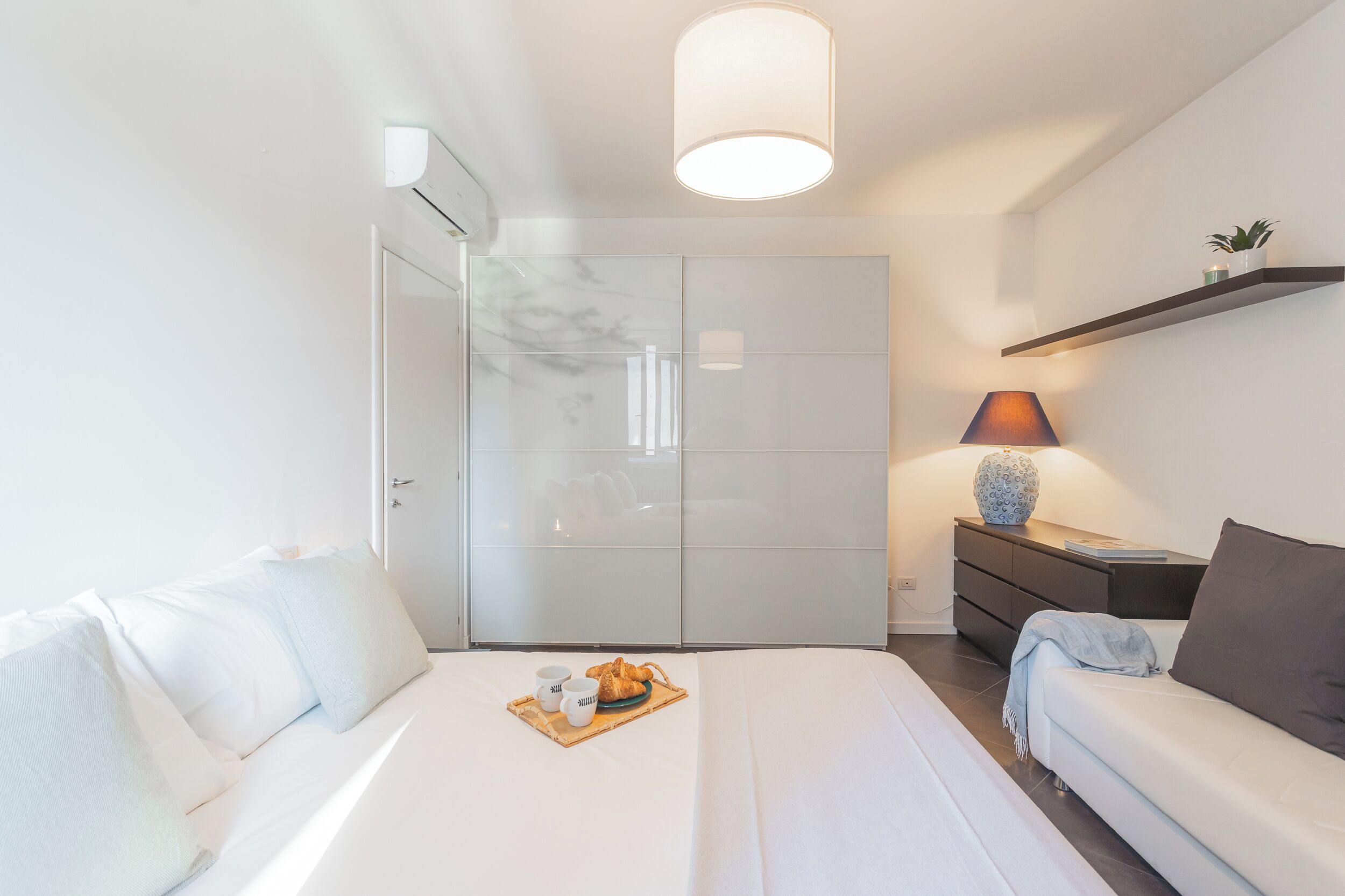 A modern bedroom with a bed, bedside table, lamp, and a wardrobe.