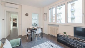 A modern living room with a dining area, a large TV, and a view of the city through large windows. - Chiara's Apartment by Rent all Como (Como)