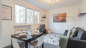 A modern living room with a dining area, featuring a black dining table, white chairs, a grey sofa, and a geometric patterned rug. - Chiara's Apartment by Rent all Como (Como)