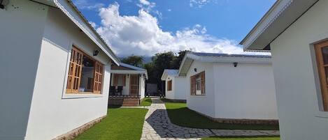 A pathway leading to a row of white buildings with wooden windows and doors, surrounded by well-maintained grass and stone paving.