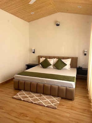 Une chambre avec un plafond en bois, un lit doté d’une tête de lit marron, deux tables de chevet et un plaid vert.