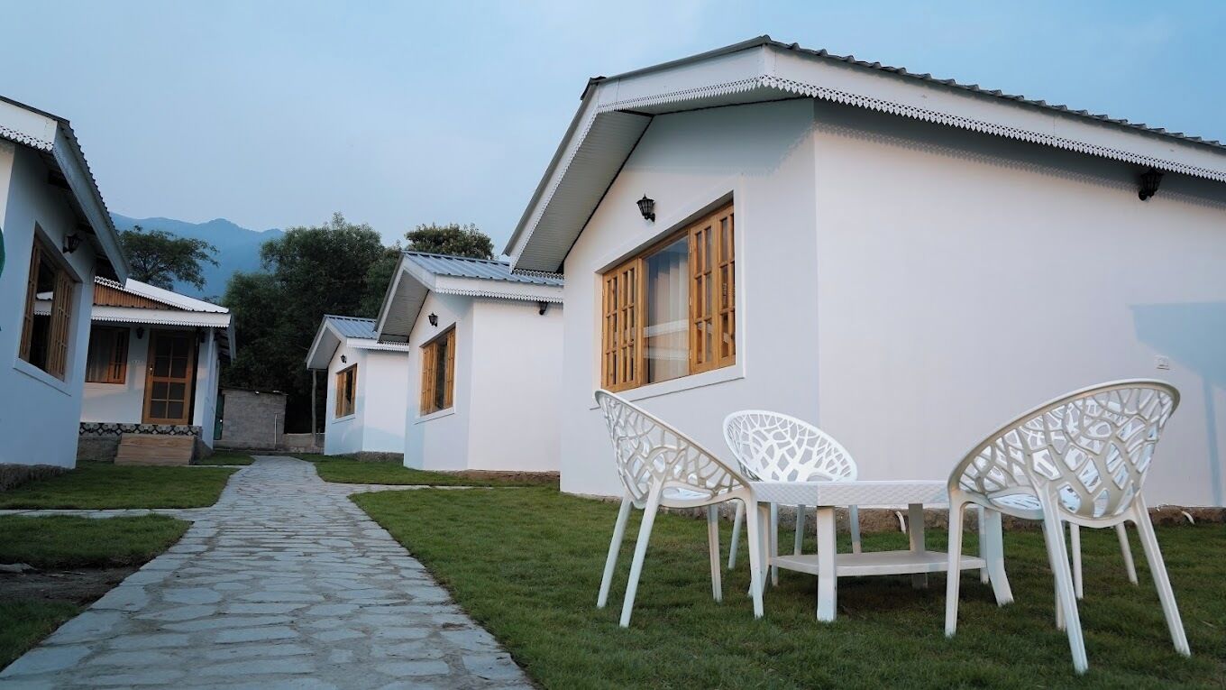 A row of white buildings with a stone pathway leading to a white table and chairs.