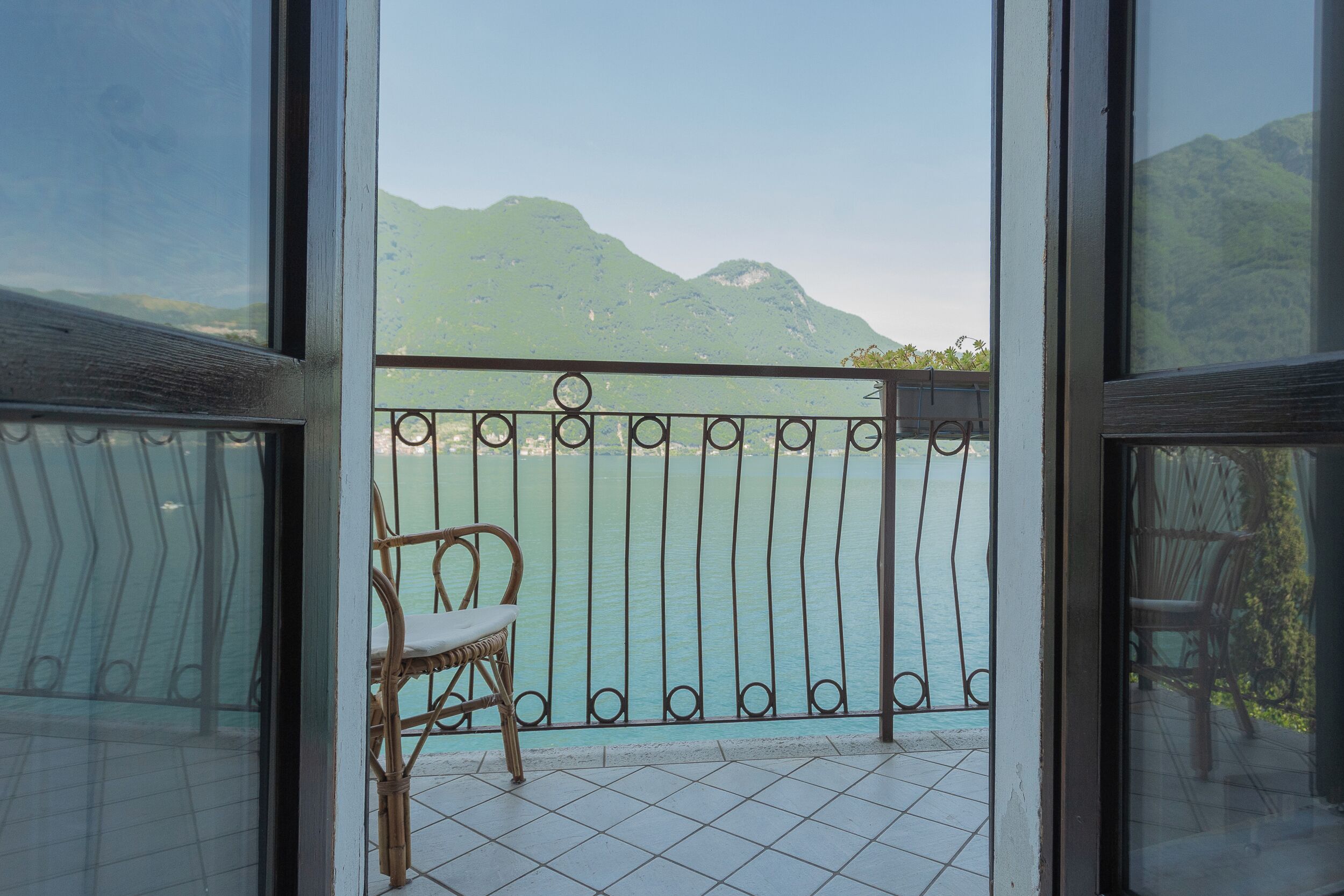 A balcony with a wicker chair, a metal railing, and a view of a mountain and water.
