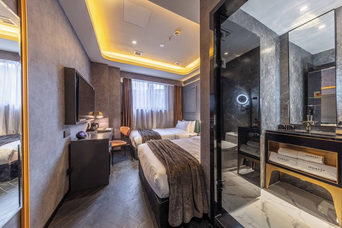 A modern hotel room with a bed, bedside table, and a desk with a chair.