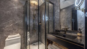 A modern bathroom with a glass-enclosed shower, a black vanity with a mirror, and marble walls. - A forest s hotel (Shanghai)
