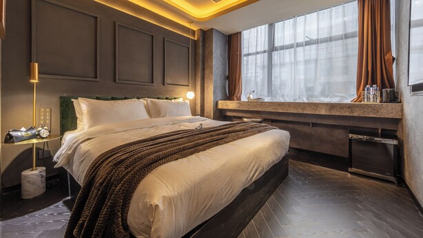 A modern hotel room with a large bed, a bedside table with a lamp, a window with curtains, and a built-in desk with a mirror. - A forest s hotel (Shanghai)