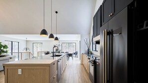 A modern kitchen with black cabinets, a central island, pendant lighting, and a view to a dining area.