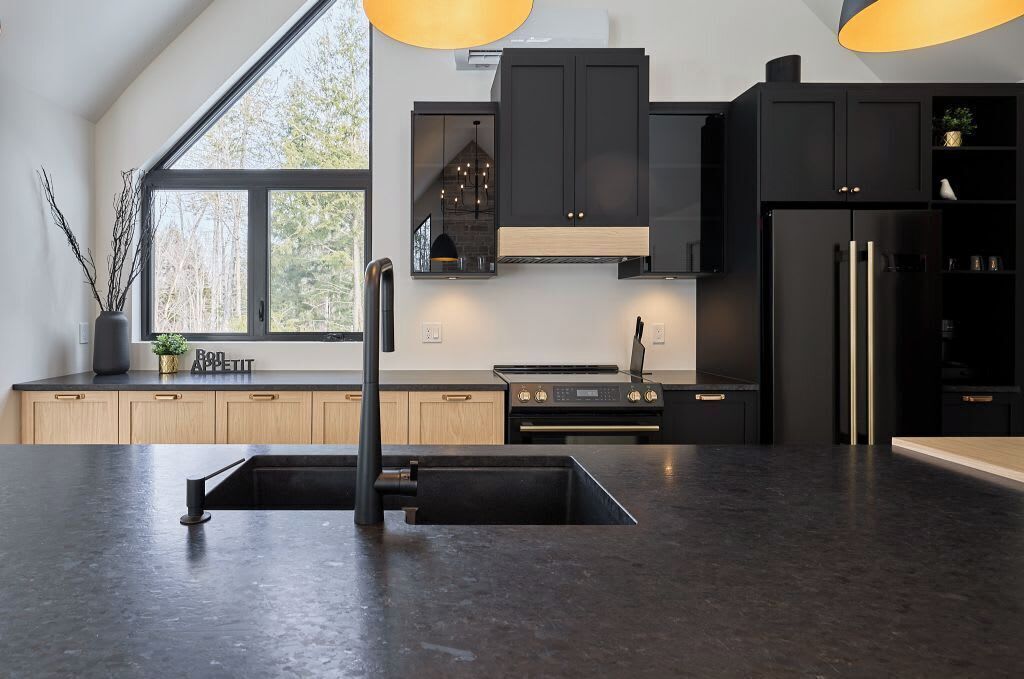 A modern kitchen with black cabinetry, a large window, and a central island.