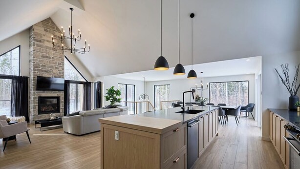 A modern kitchen with a central island, pendant lighting, and a stone fireplace.