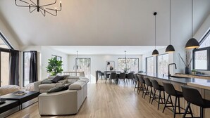 A modern living room with a sofa, dining area with chairs, and a kitchen with bar stools.