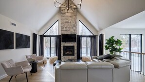 A spacious living room with a stone fireplace, large windows, and a modern chandelier.