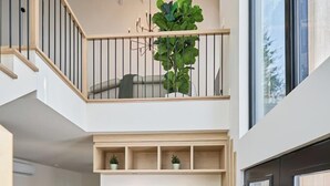 A spacious interior with a wooden staircase, a seating area with a bench, and a large window providing a view of the outdoors.