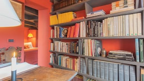 A room with a bookshelf filled with books, a wooden table with a candle, and a lamp. - La Corte Degli Artisti by Rent all Como (Blevio)