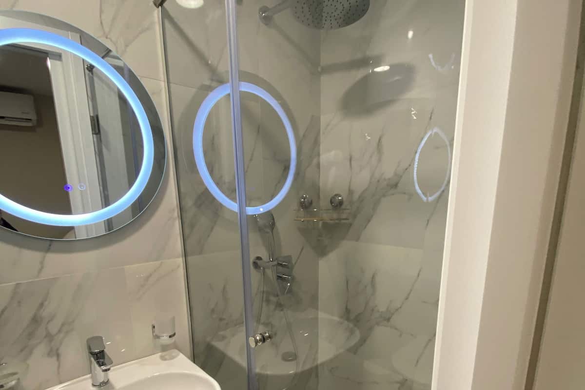 Een moderne badkamer met een douchecabine van glas, een ronde spiegel met verlichting en een wand betegeld met marmer.