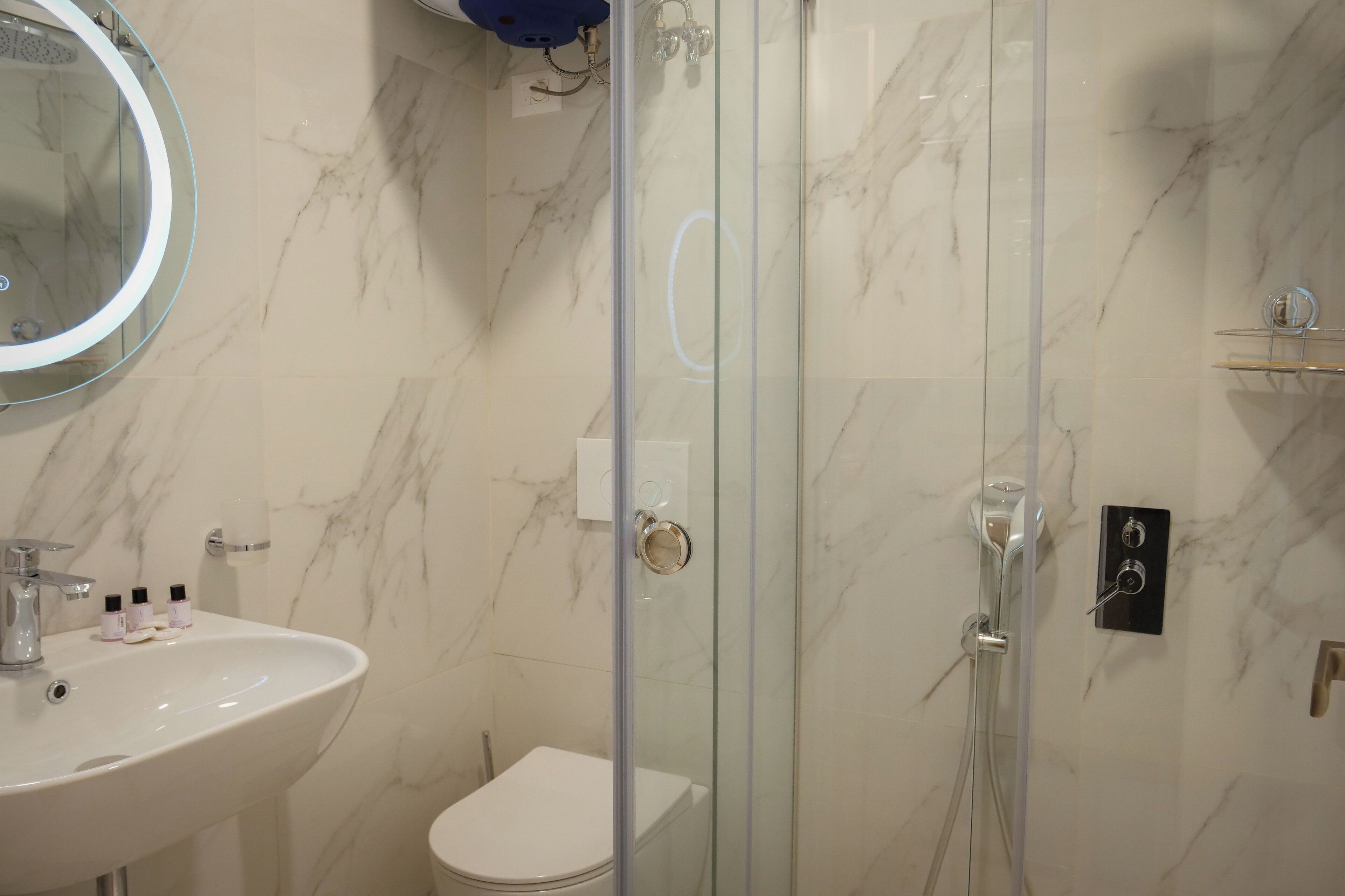 A bathroom with a marble wall, a glass-enclosed shower, a white sink, and a toilet.