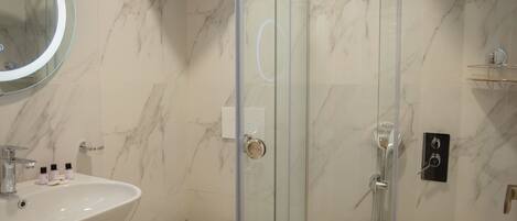 A bathroom with a marble wall, a glass-enclosed shower, a white sink, and a toilet.