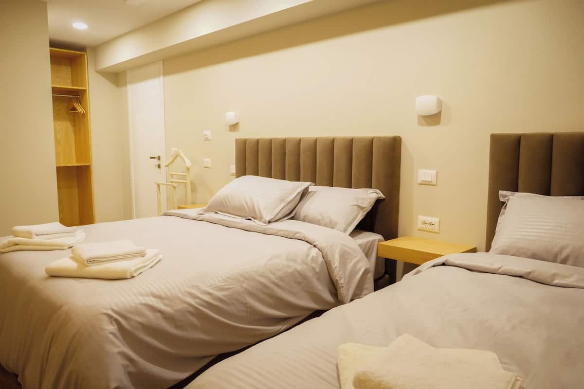 Een hotelkamer met twee bedden, een houten garderobe en een kleine tafel met een lamp.