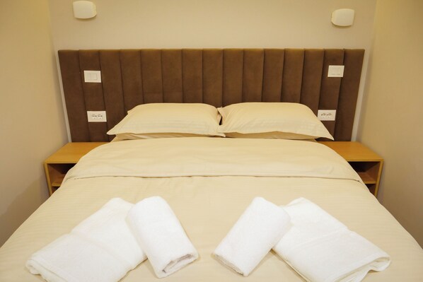 A neatly made bed with a brown headboard, two pillows, and two folded towels on the bed.