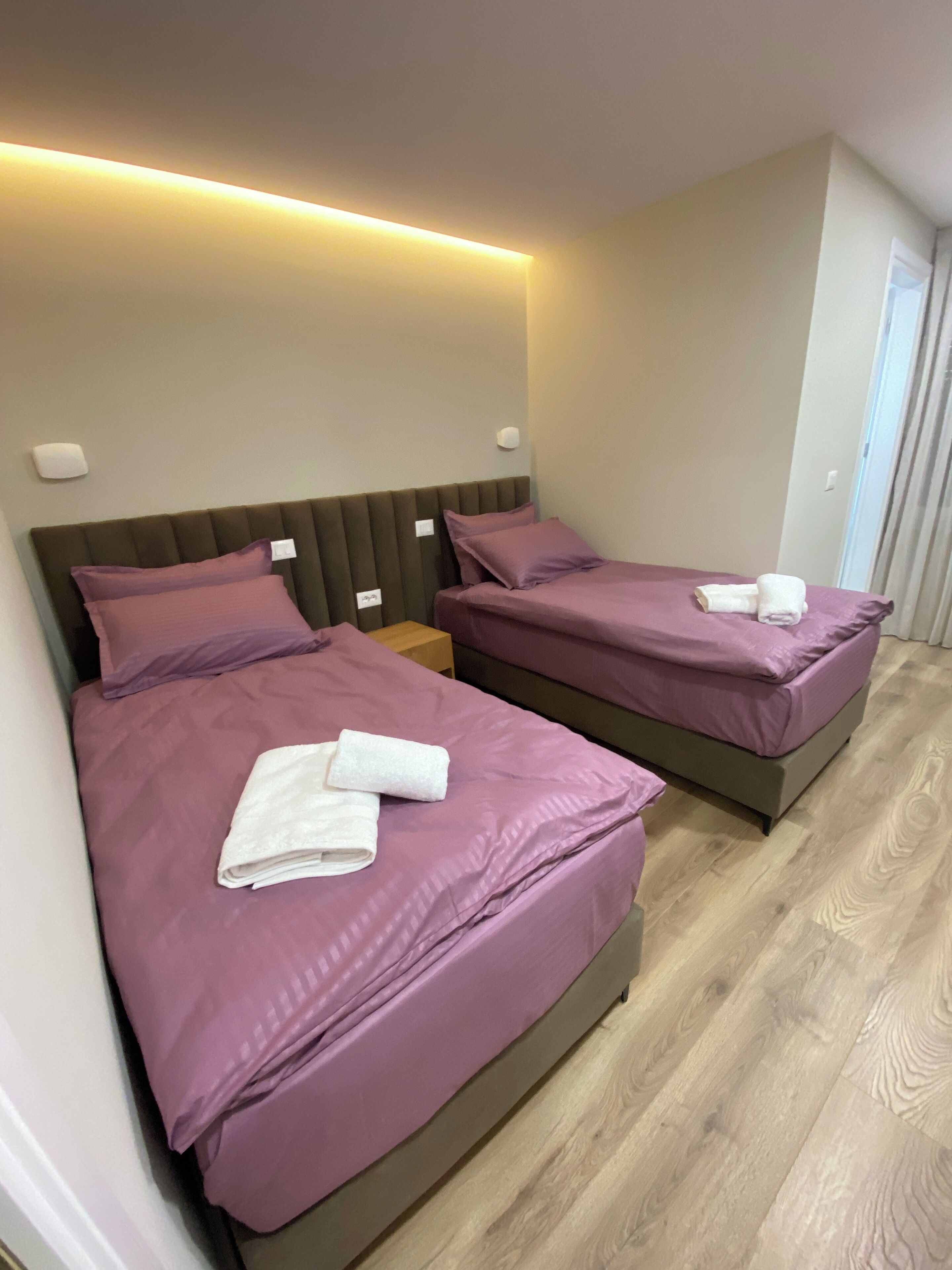 Ein Hotelzimmer mit zwei Betten, jeweils mit violetter Bettwäsche und weißen Handtüchern.