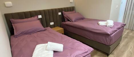 Ein Hotelzimmer mit zwei Betten, jeweils mit violetter Bettwäsche und weißen Handtüchern.