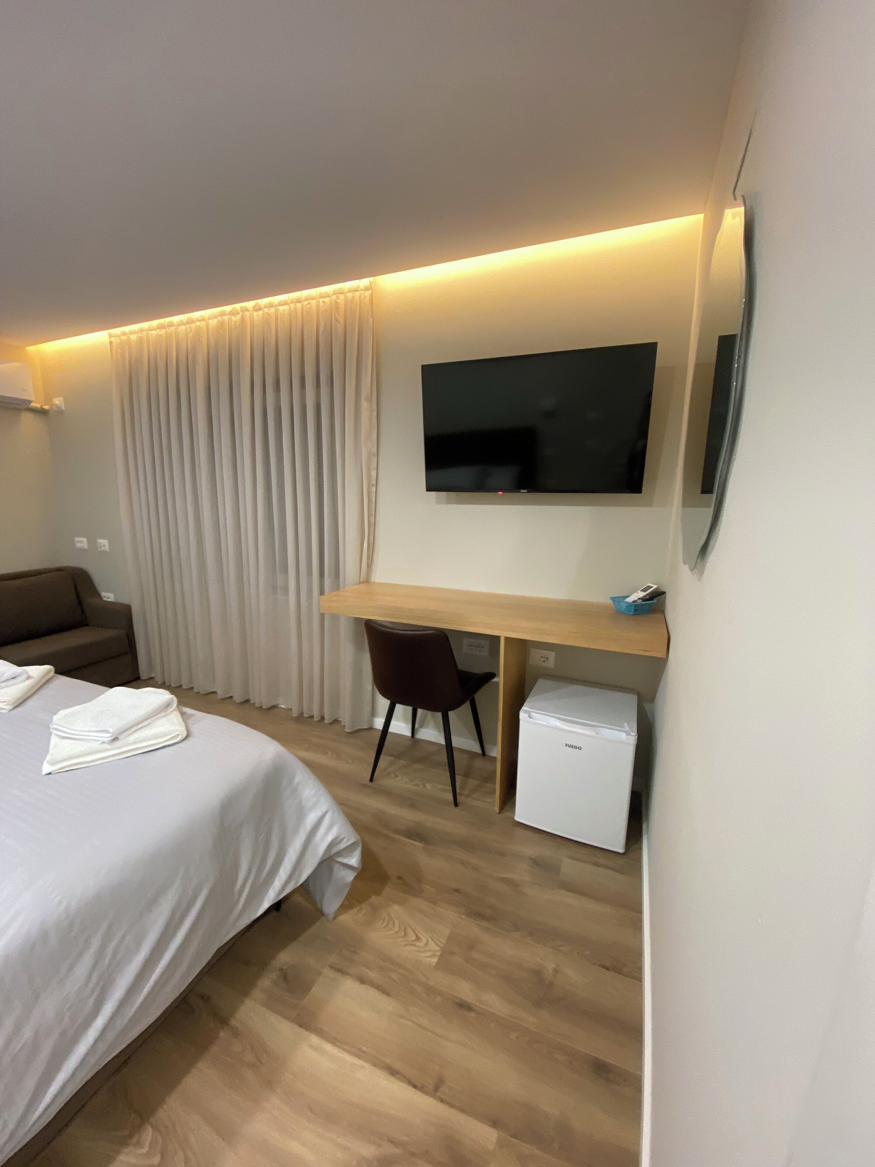 A hotel room with a bed, a desk, a chair, a TV, and a mini-fridge.