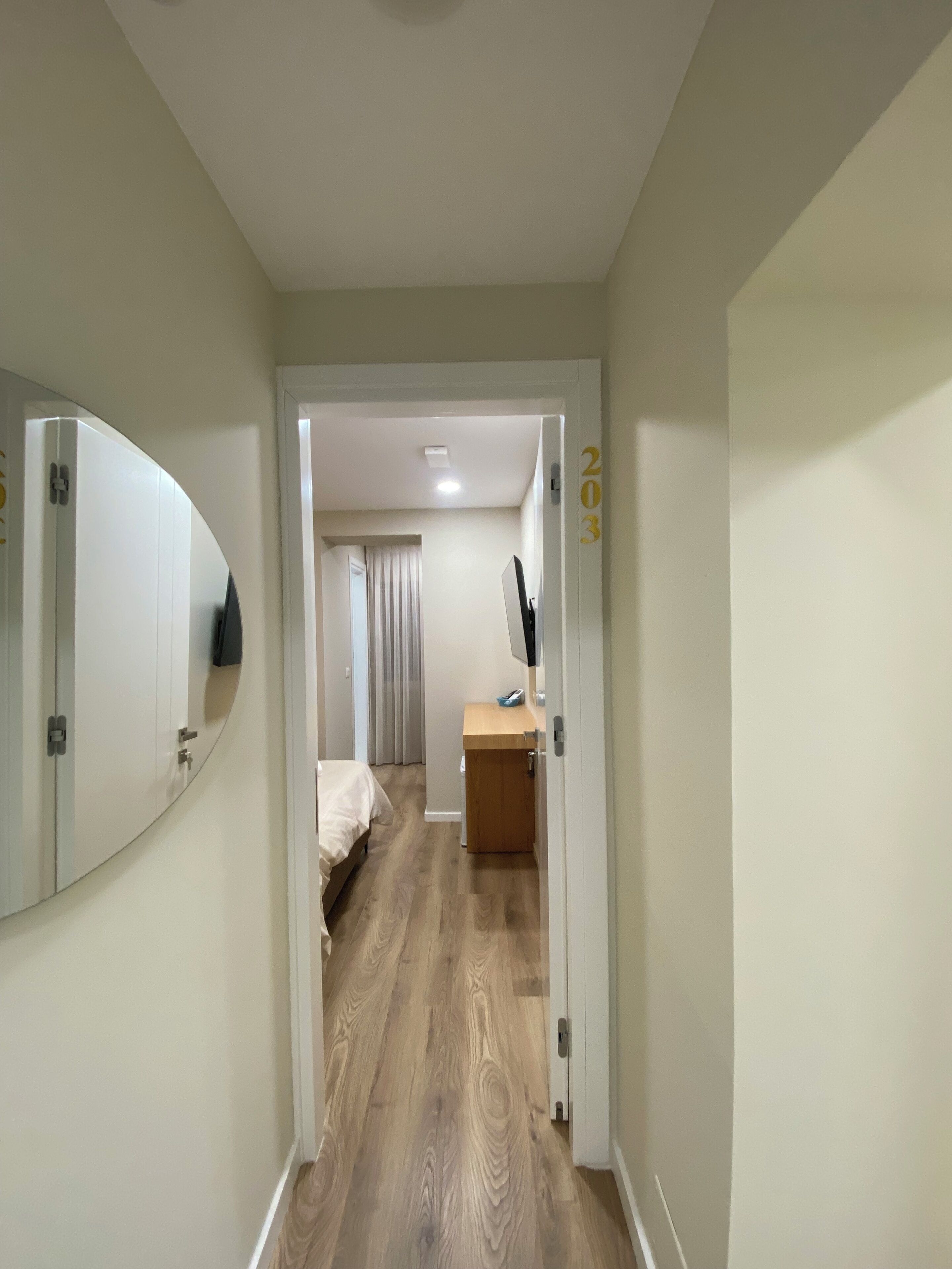 A hallway leading to a bedroom with a bed, a desk, and a mirror.