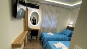 Une chambre d’hôtel avec un bureau en bois, un miroir, un lit avec une literie bleue et un luminaire au plafond.